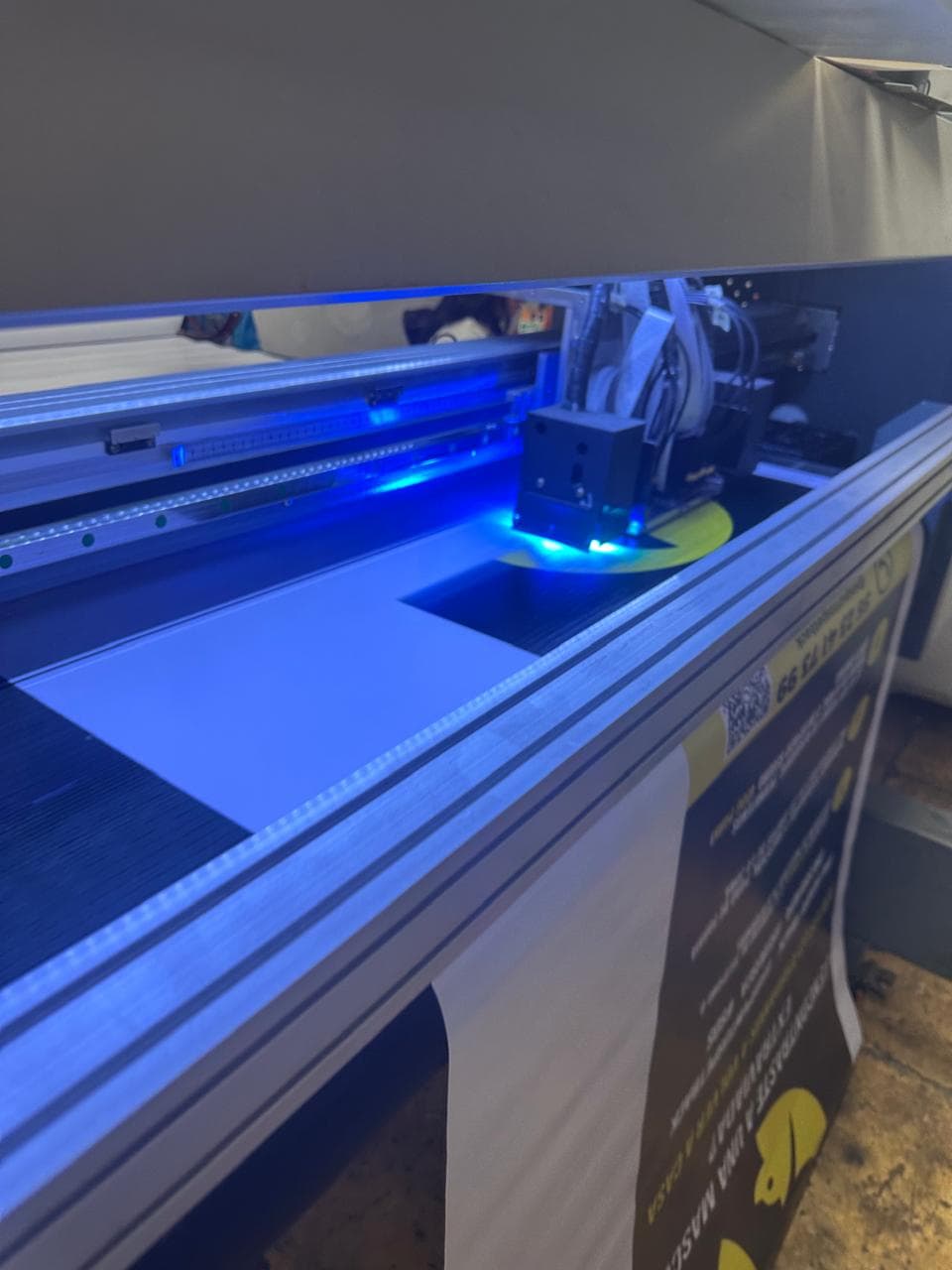 UV printer head with bright blue light printing a yellow graphic on white material.
