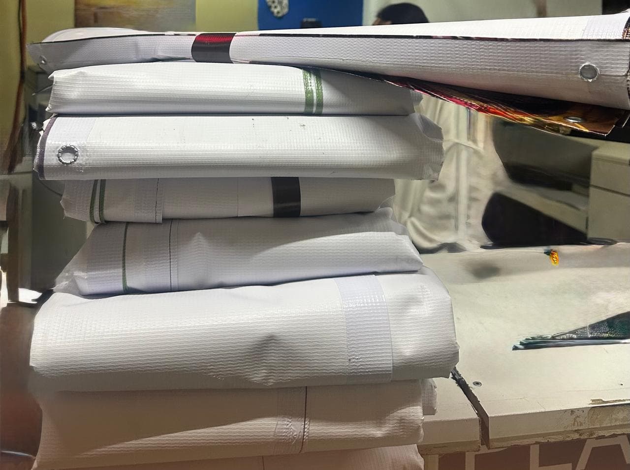 Neatly stacked white vinyl banners featuring metal grommets and colored tape on a workshop table.